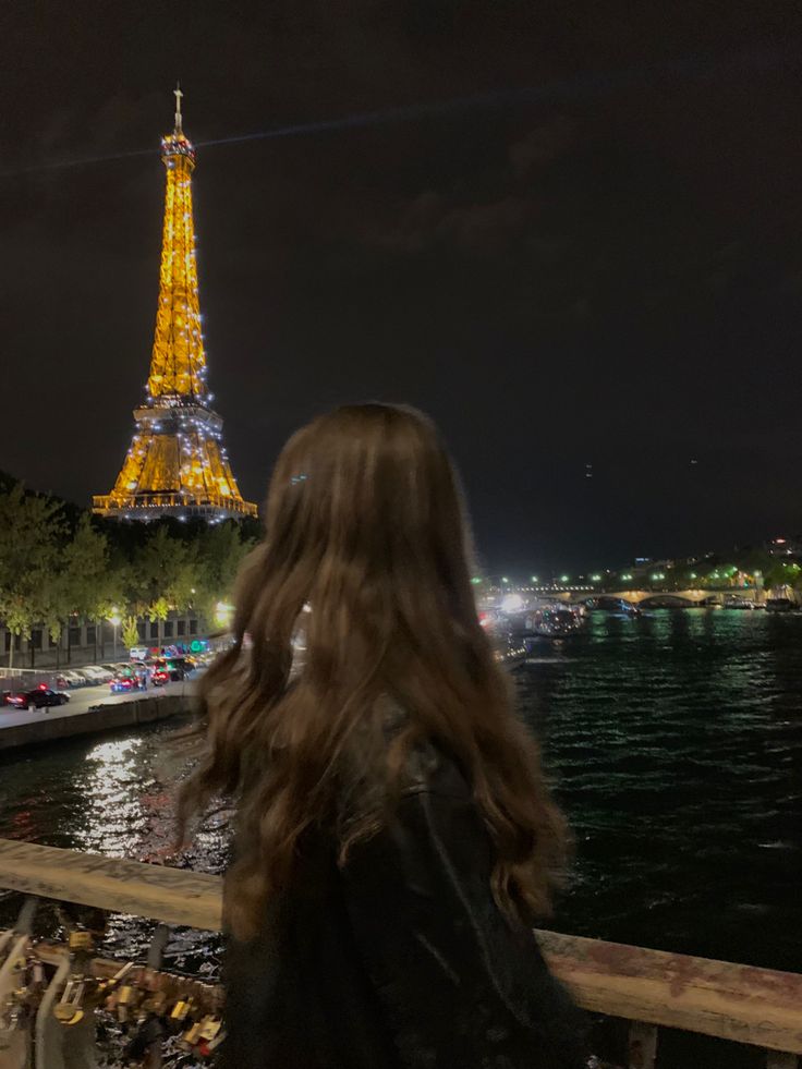 a woman looking at the eiffel tower from across the river in paris, france