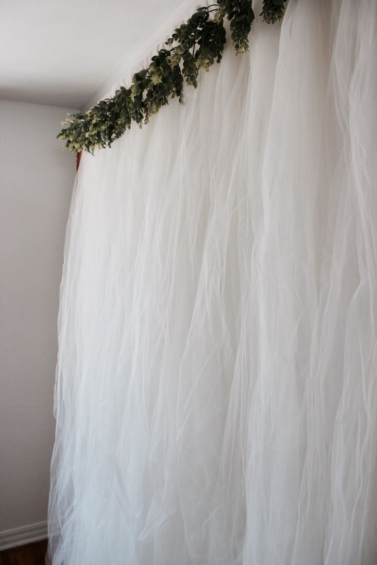 the curtain is covered with white tulle and greenery hanging from it's side