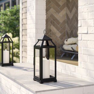 two black lanterns sitting on top of a window sill next to a white brick wall