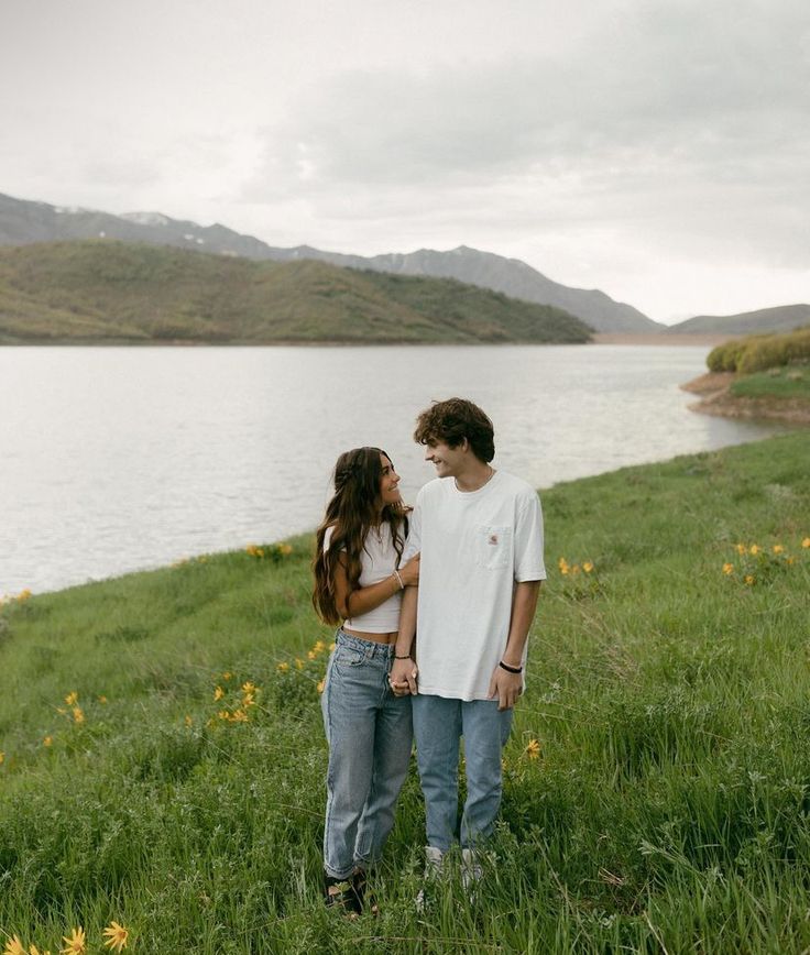 a man and woman standing next to each other in front of a body of water