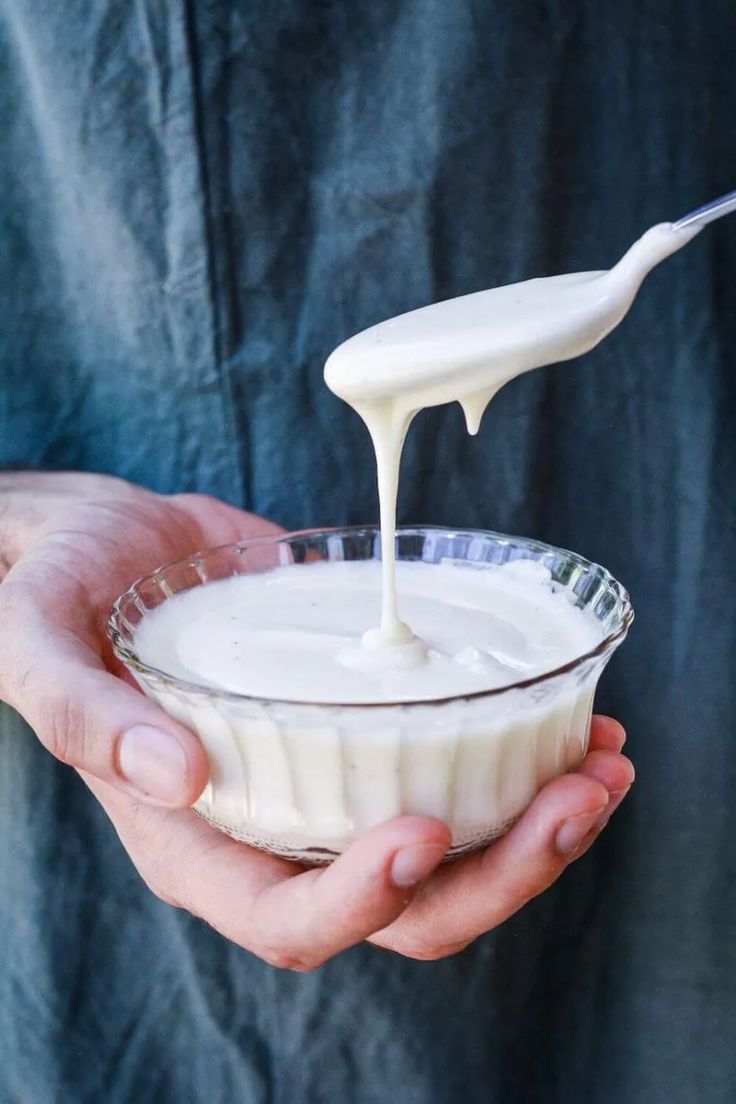 a person holding a glass bowl filled with yogurt and a spoon in it