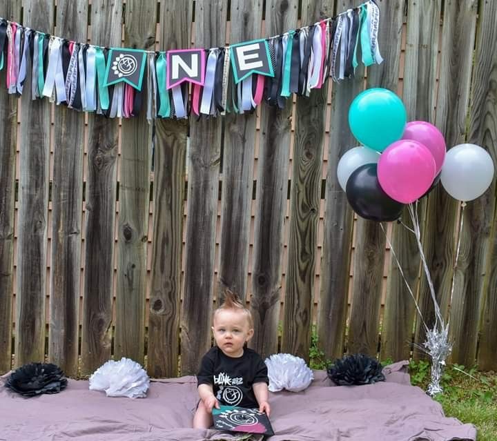 a baby sitting on a blanket in front of a fence with balloons and streamers