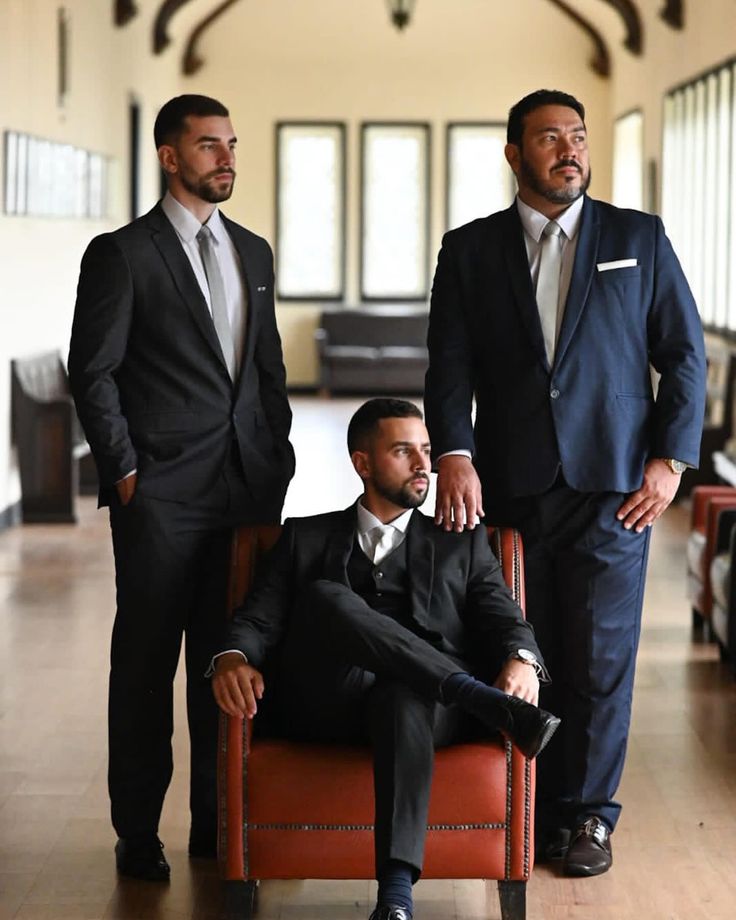 two men in suits are sitting on a red chair and one man is standing behind them