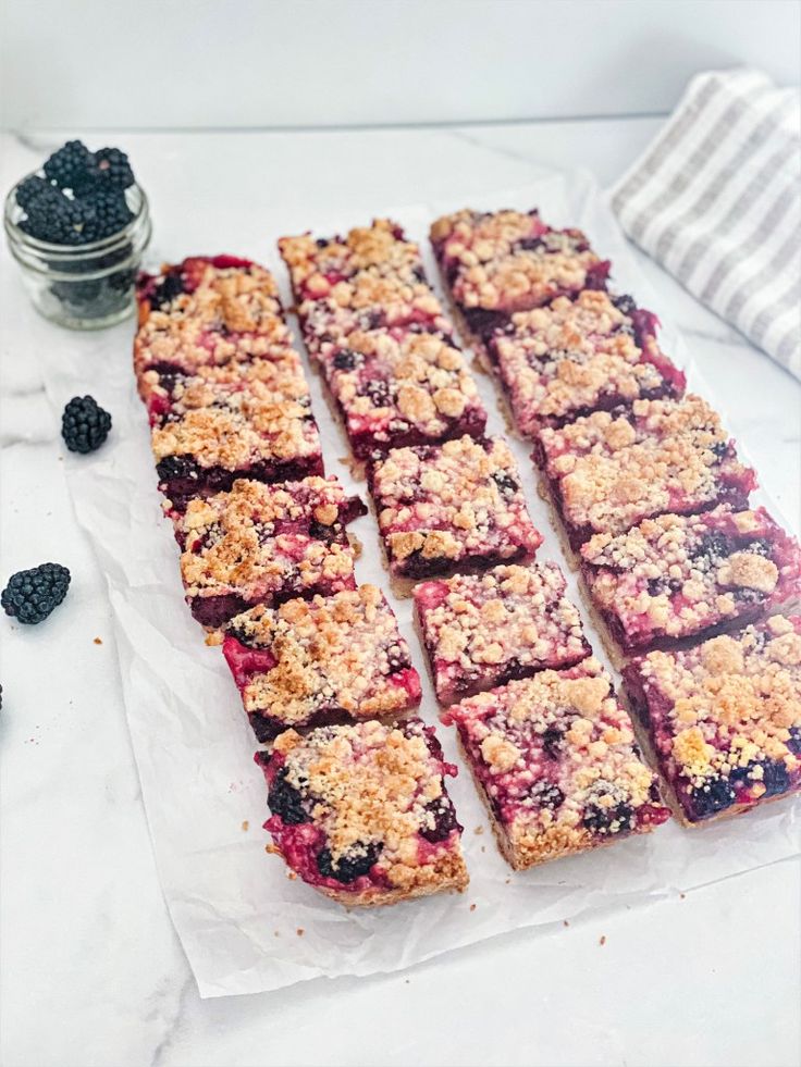 blueberry crumble bars cut into squares on top of a white table next to some blackberries