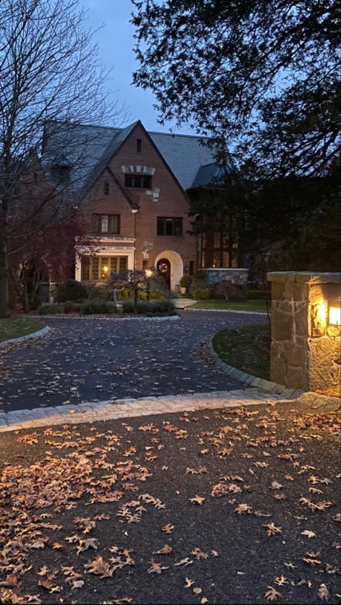 a large house lit up at night with lights on it's front door and driveway