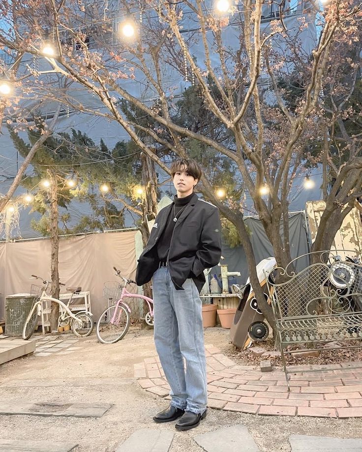 a man standing in front of a tree with lights strung from it's branches