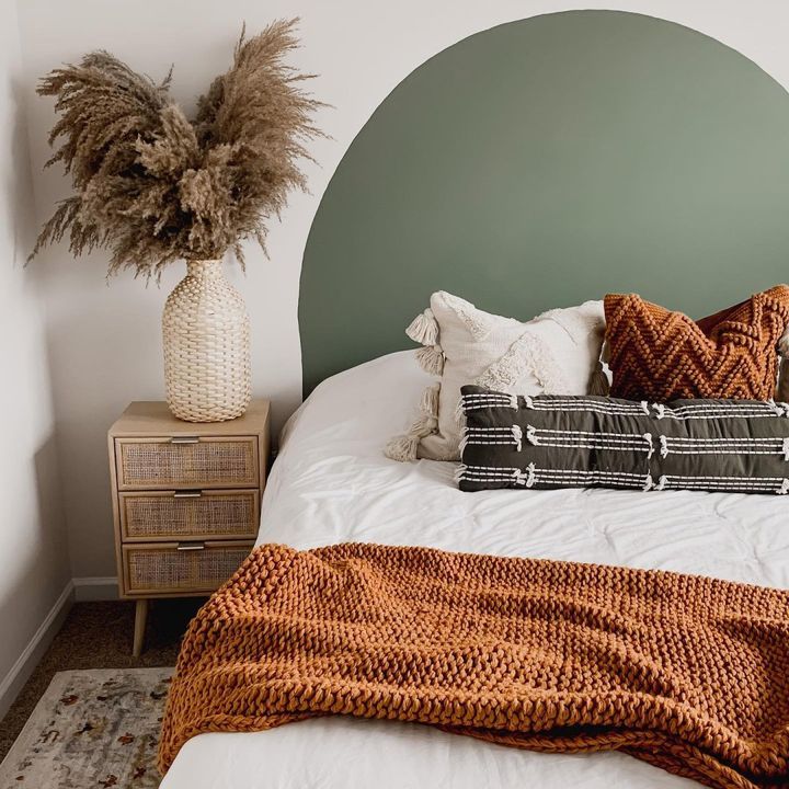 a bed with pillows and blankets on it in front of a green headboard that is next to a plant