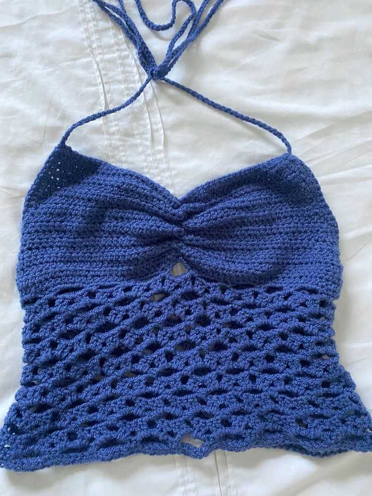 a crocheted blue top with a bow on the front and back, sitting on a bed