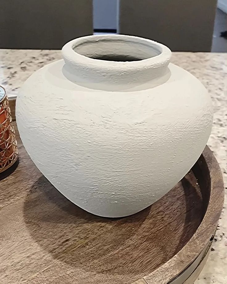 a large white vase sitting on top of a wooden table next to a jar filled with honey