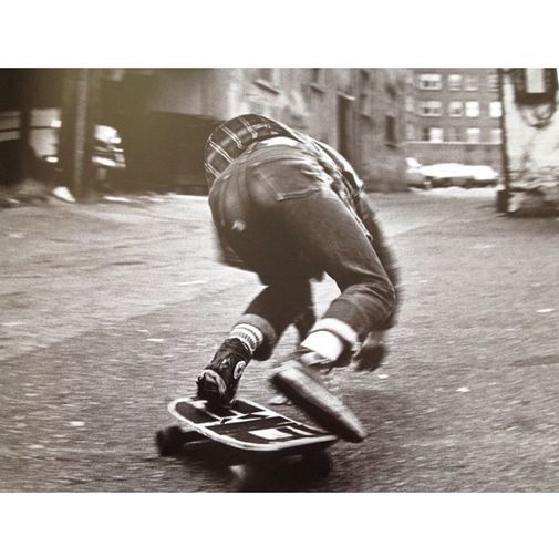 a man riding a skateboard down a street next to tall buildings on either side