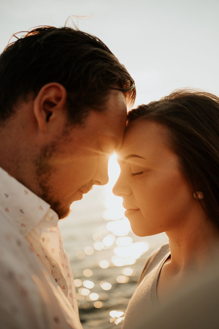 a man and woman standing next to each other in front of the ocean at sunset