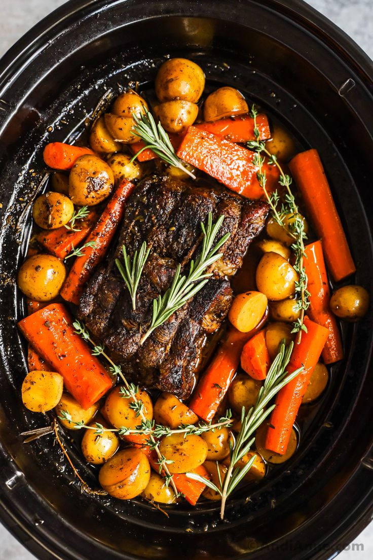 a pot roast with carrots, potatoes and rosemary garnish on the side