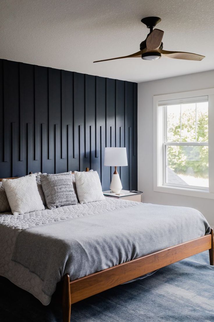 a large bed sitting under a window in a bedroom next to a wall mounted fan