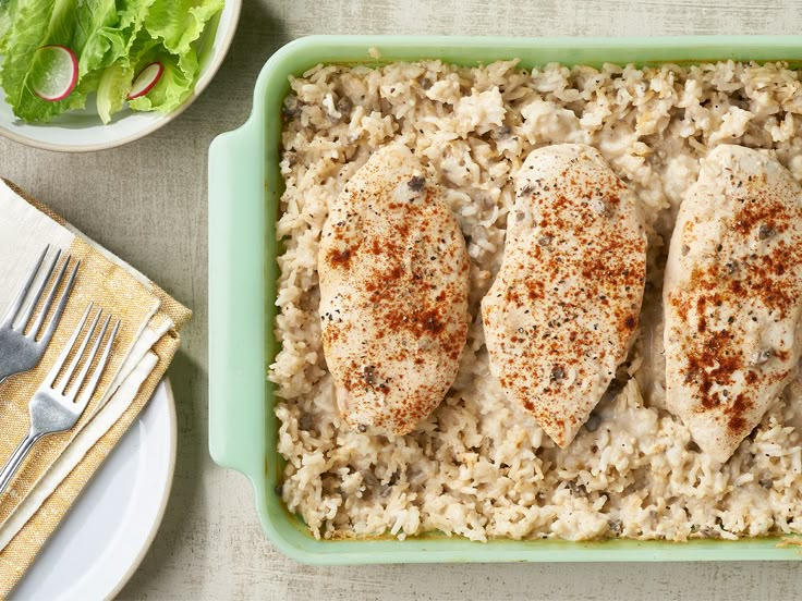 chicken and rice in a green casserole dish on a table with silverware