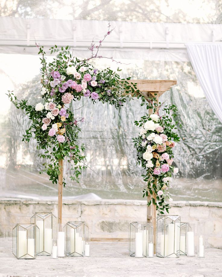 the wedding arch is decorated with pink and white flowers, greenery and candles for an outdoor ceremony