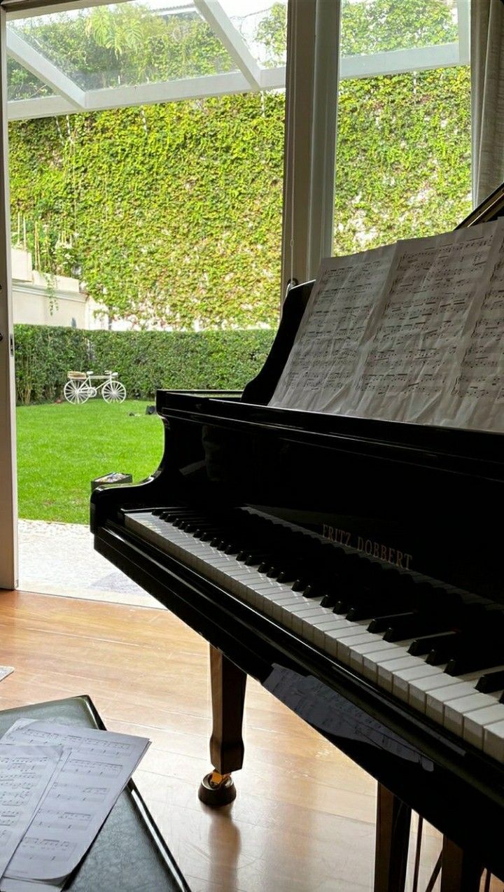 a piano sitting on top of a hard wood floor in front of a window next to a green wall