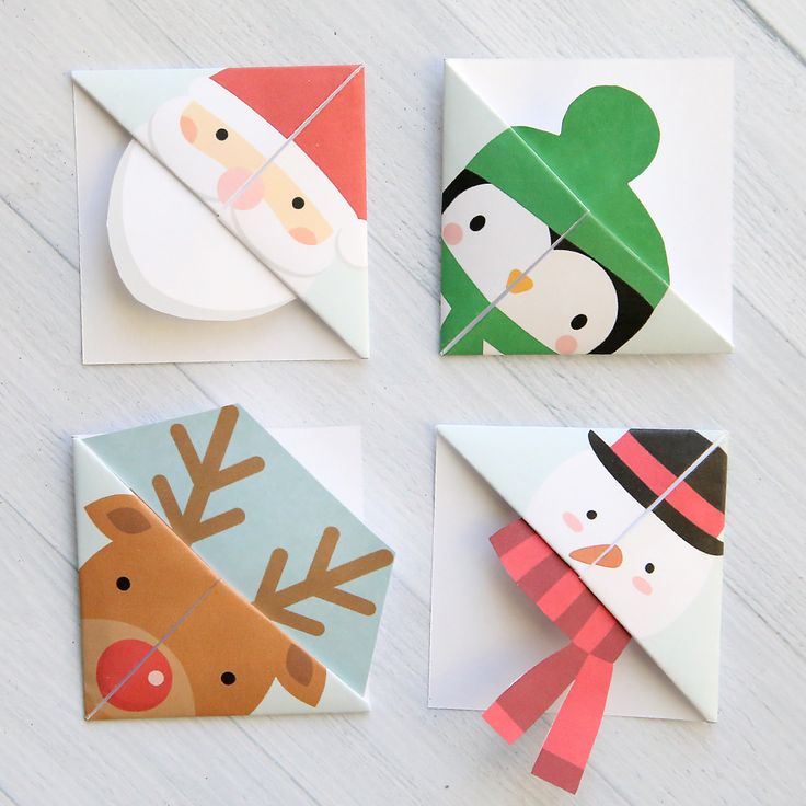 four folded christmas cards with paper snowmen, reindeer and santa hats on them sitting on a white wooden surface