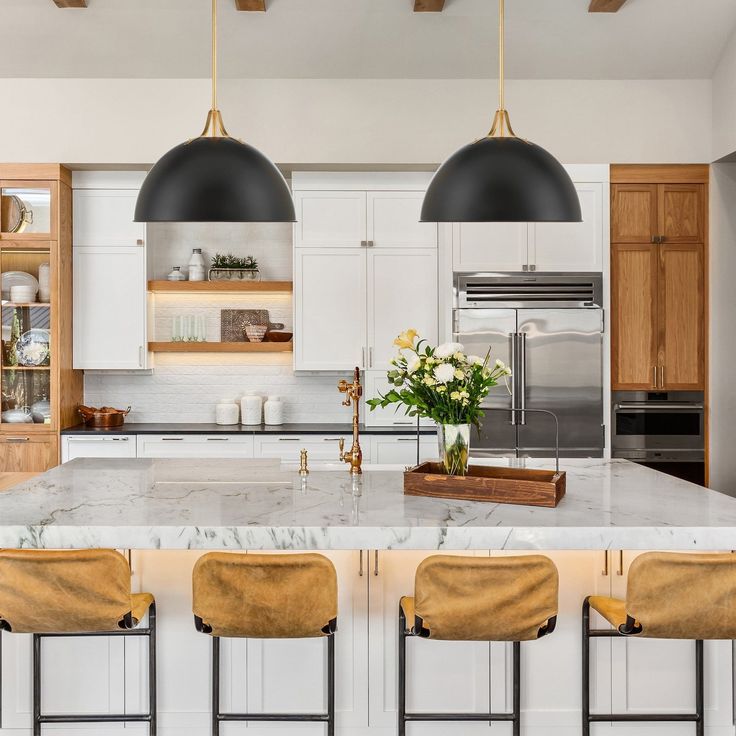 a kitchen with marble counter tops and two pendant lights hanging over the island, along with three bar stools