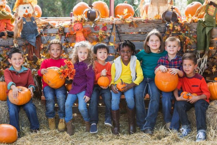 a group of children holding pumpkins in front of hay bales with decorations on them