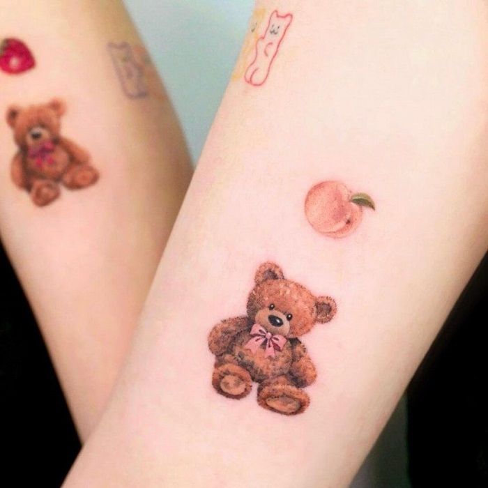 two small tattoos on the arms of girls with teddy bears and peaches painted on them