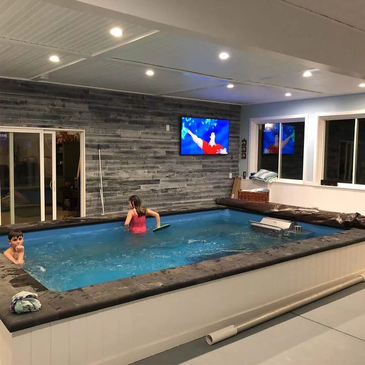 two people sitting in an indoor swimming pool with tvs on the wall behind them