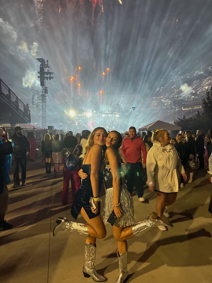 two young women standing in front of fireworks at an outdoor event with their arms around each other