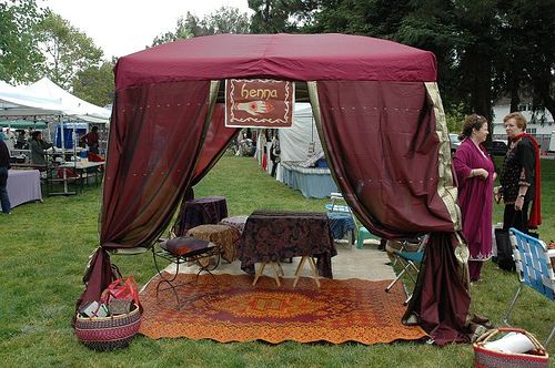 an outdoor tent set up on the grass with people standing around it and tents in the background