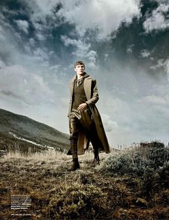 a man standing on top of a grass covered field next to a mountain under a cloudy sky