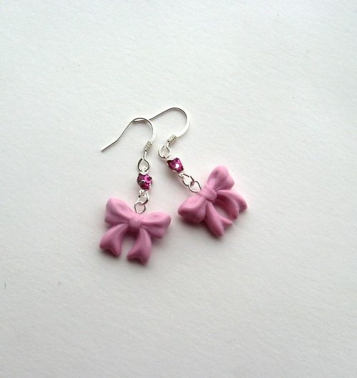 two pink bows are hanging from silver earwires on a white surface with beads