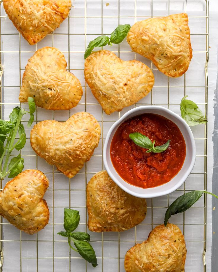 several pastries and a bowl of tomato sauce on a cooling rack with basil leaves