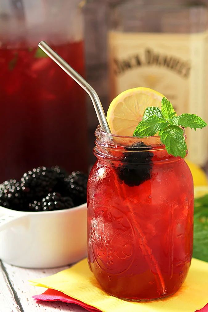 a mason jar filled with blackberries, lemon and mint next to a bowl of berries