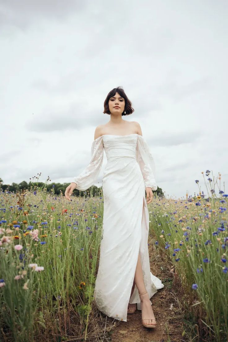 a woman in a white dress is standing in the middle of a field with wildflowers