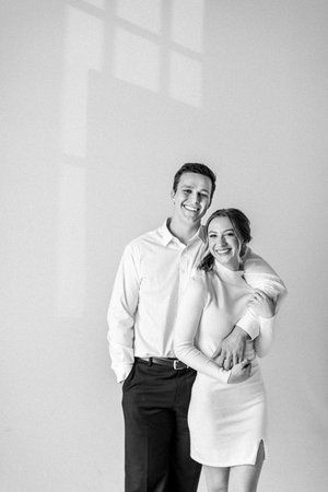 a man and woman standing next to each other in front of a white wall smiling at the camera