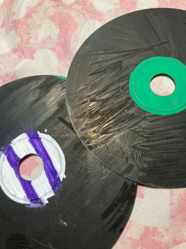 two black discs with purple and white designs on them, one has a green circle