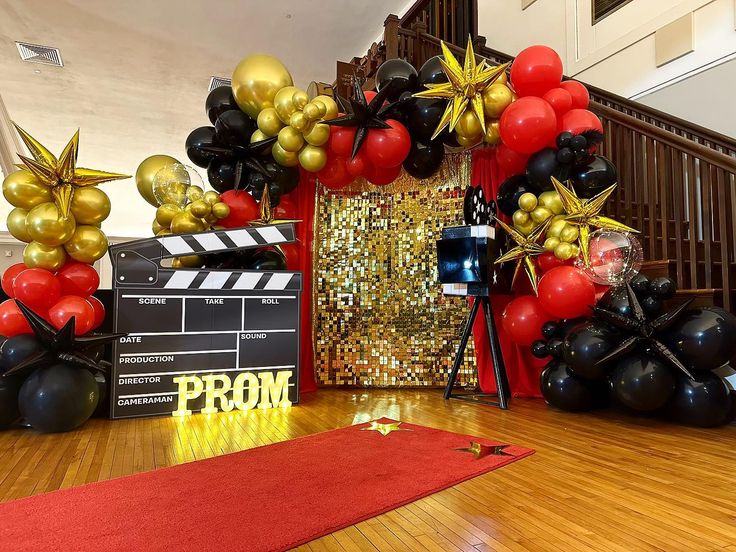 some black and gold balloons are in front of a red carpeted area with a movie claper