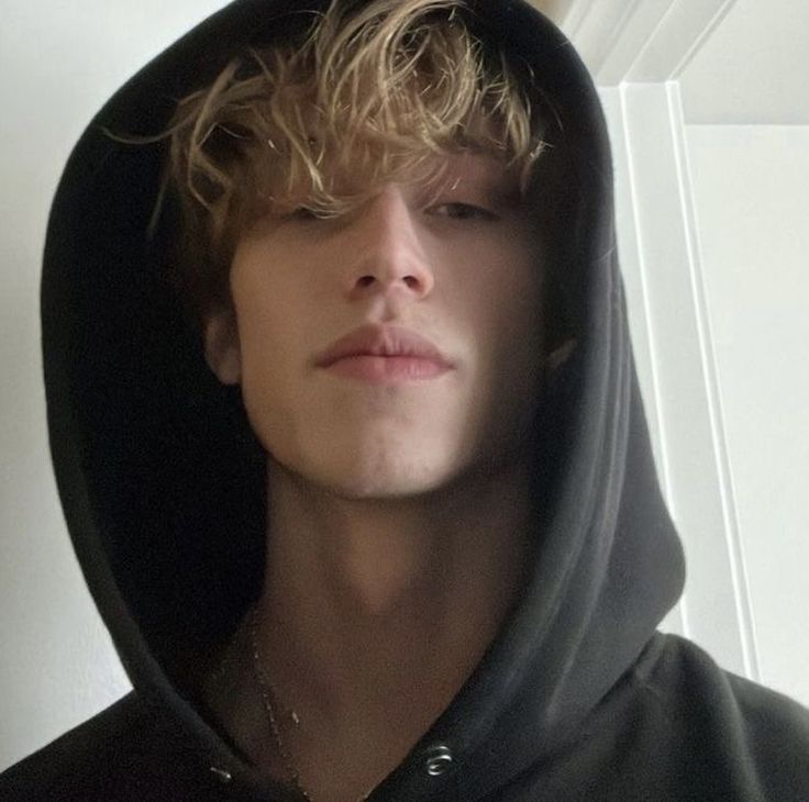 a young man with blonde hair wearing a black hoodie and looking at the camera