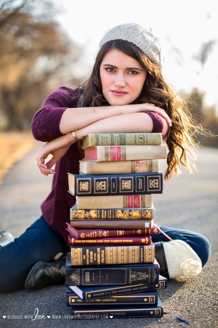 a young woman sitting on the ground next to a stack of books with her arms crossed