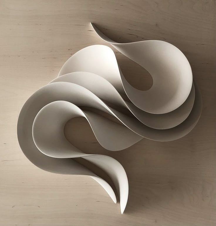 an abstract sculpture made out of white paper on top of a wooden surface with no one in it