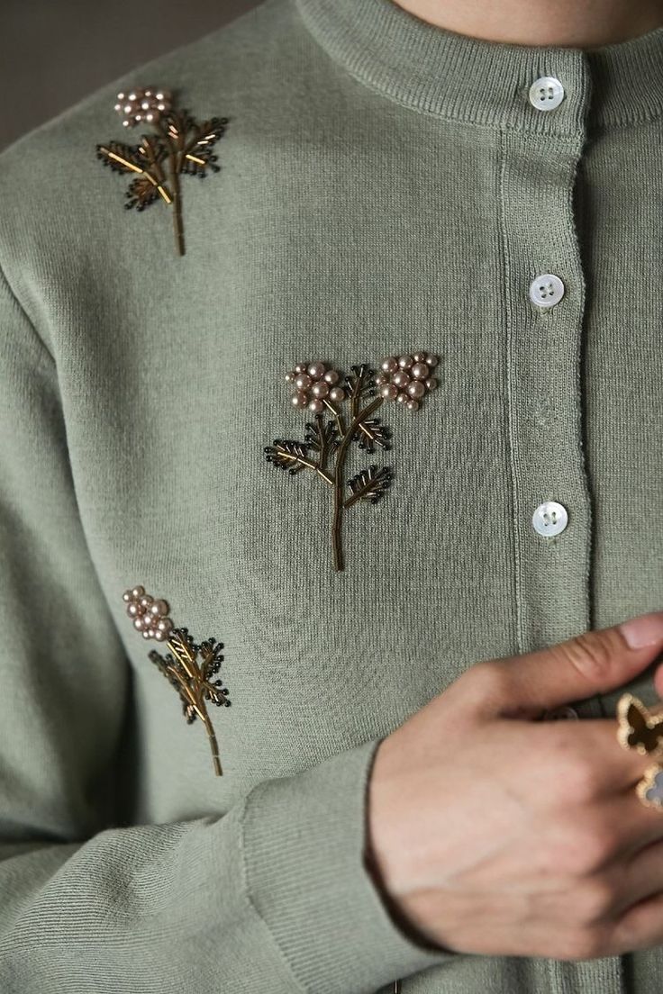 a person wearing a green sweater with flowers on it and buttons in the middle of their sleeves