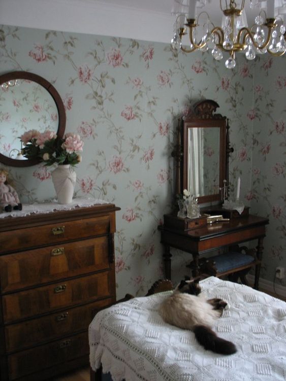 a cat laying on top of a bed next to a dresser with a mirror and chandelier