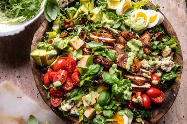 a salad with chicken, avocado and tomatoes in a wooden bowl on a table