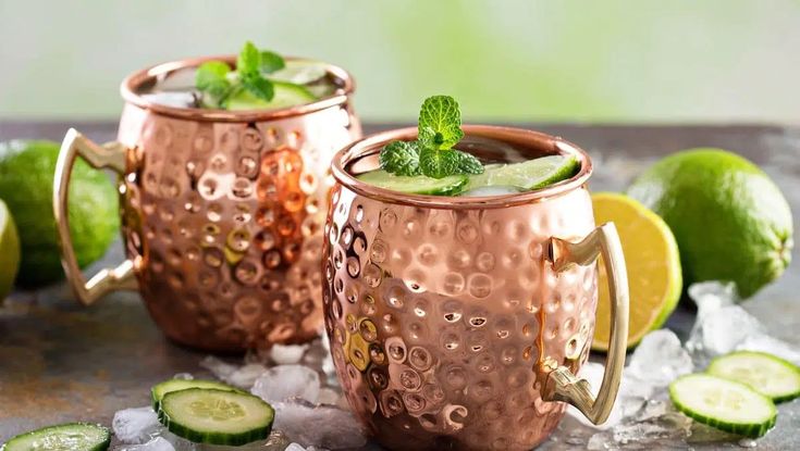 two copper mugs filled with cucumber and mint garnish on top of ice