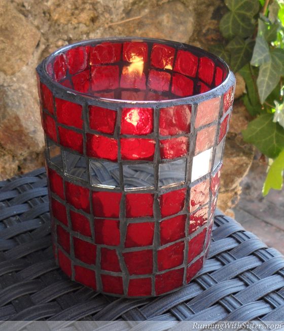 a red glass candle holder sitting on top of a table next to a stone wall