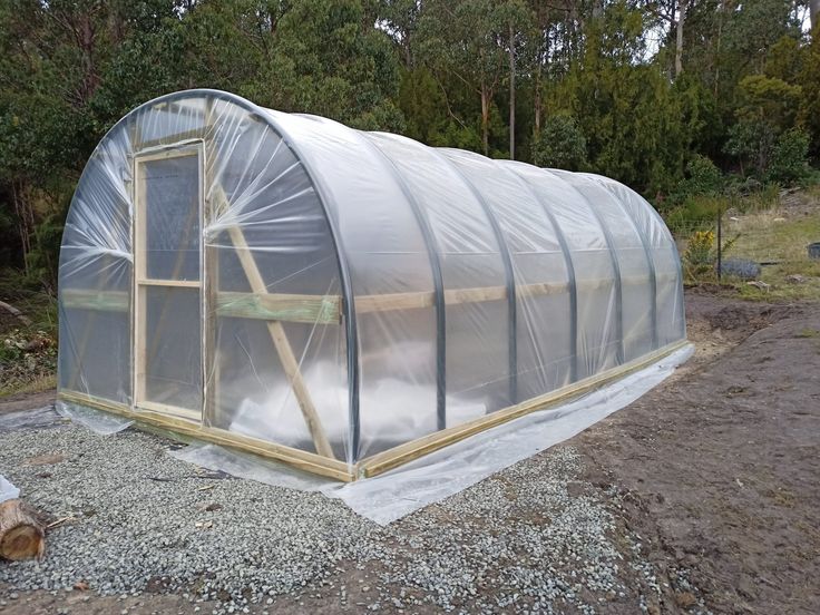 a small greenhouse is being built in the middle of some gravel and trees behind it