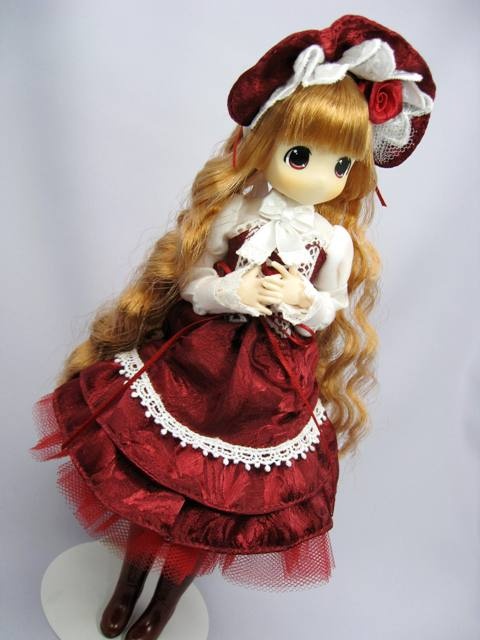 a doll with long hair wearing a red dress and white bonnet is sitting on a stand