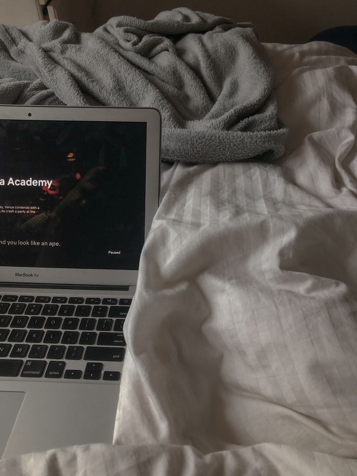 an open laptop computer sitting on top of a bed next to a white comforter