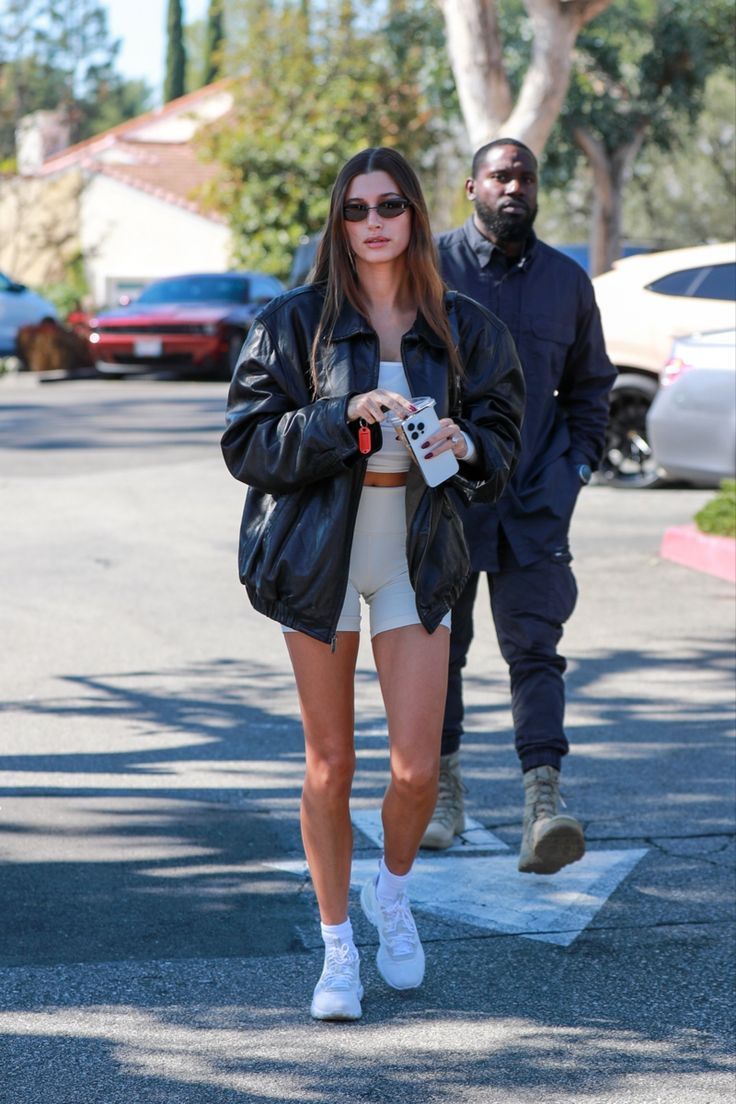 a woman walking down the street while holding a coffee cup in her hand and wearing white sneakers