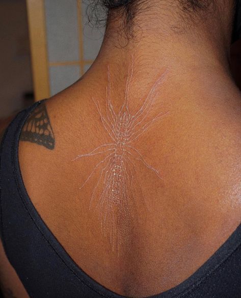 the back of a woman's neck with an intricate tattoo design on her left shoulder