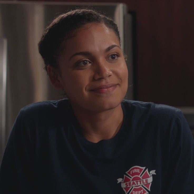 a woman sitting in front of a refrigerator wearing a black shirt with the words fire department on it