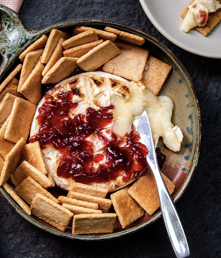 a plate with crackers, cheese and jam on it next to a bowl of crackers